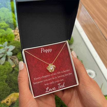 Gold necklace in a red box with a message, held by a hand outdoors.